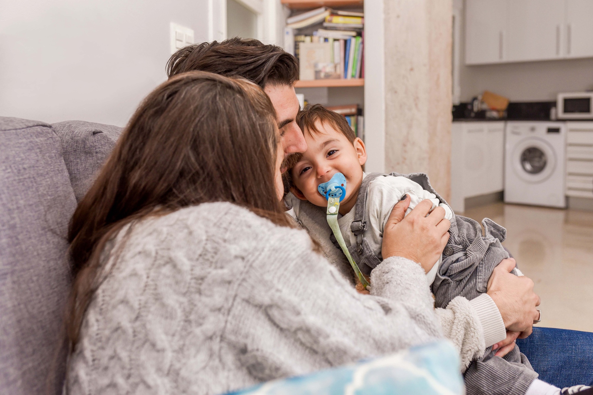 Happy family hugging and playing with their baby son while sitting on the sofa at home